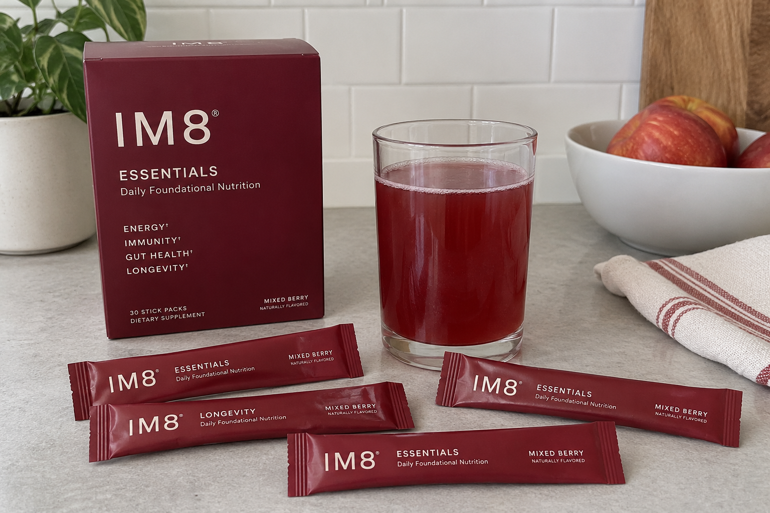 IM8 Essentials and Longevity supplement packaging with stick packs and a prepared red mixed berry drink on a kitchen counter