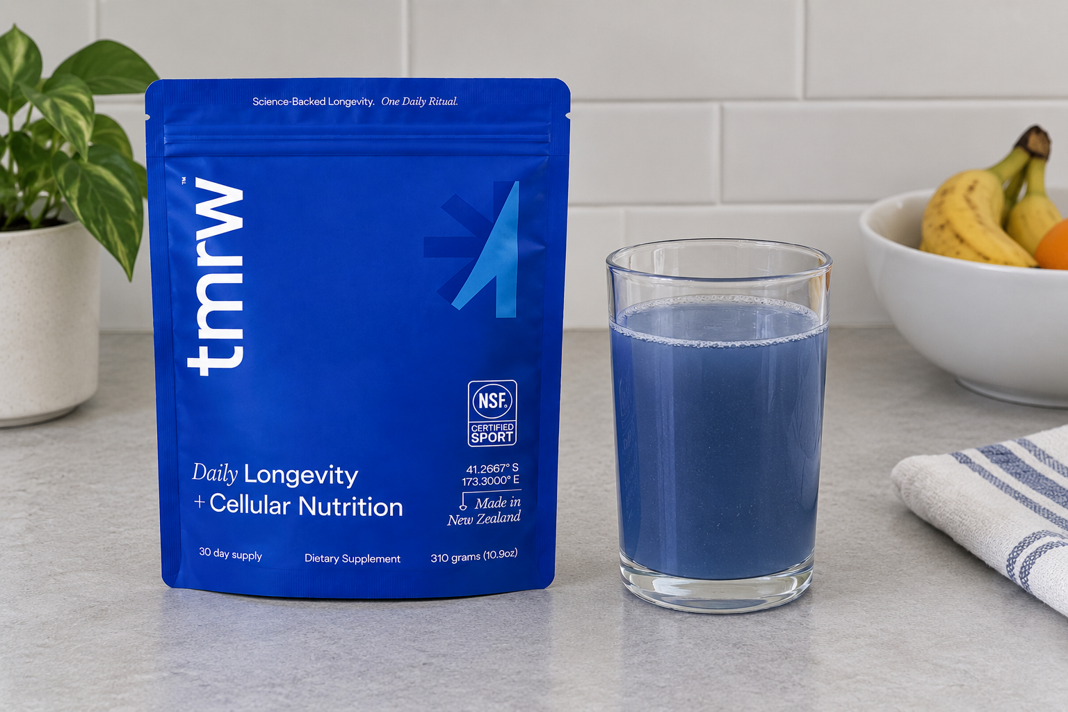 Tmrw Daily Longevity blue supplement pouch with a prepared blue drink in a clean contemporary setting